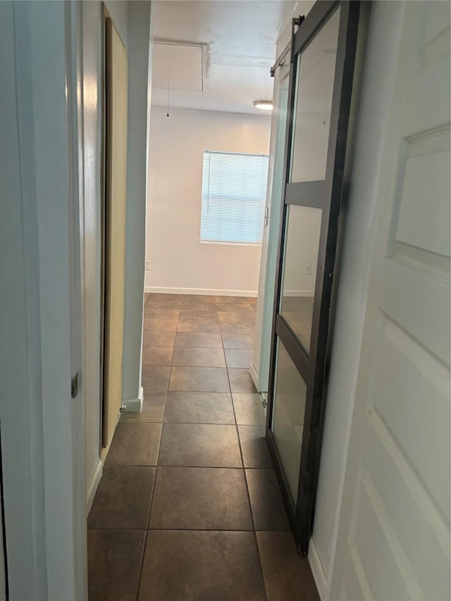 hallway with a barn door and dark tile patterned flooring