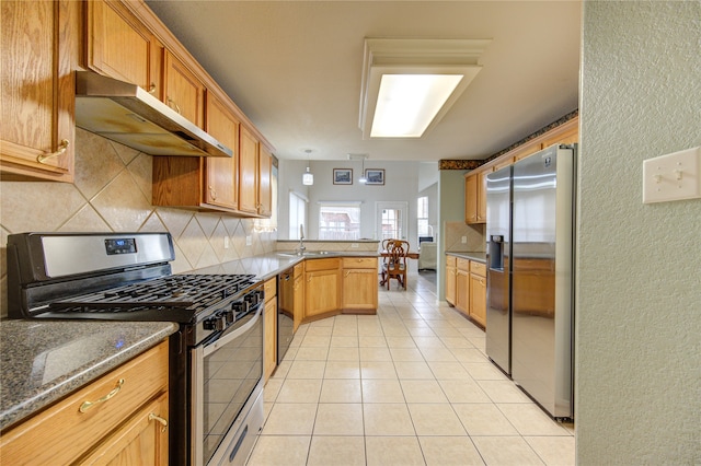 kitchen with dark stone counters, sink, light tile patterned floors, appliances with stainless steel finishes, and kitchen peninsula