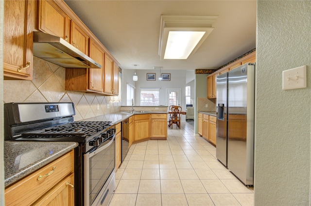 kitchen with kitchen peninsula, appliances with stainless steel finishes, dark stone counters, sink, and light tile patterned floors