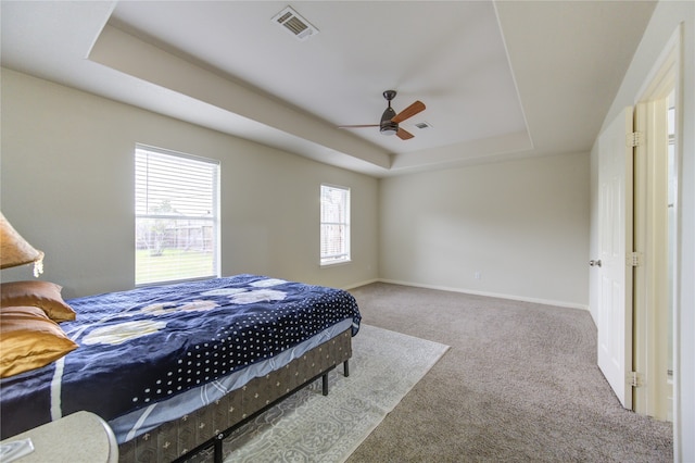 carpeted bedroom with a raised ceiling and ceiling fan