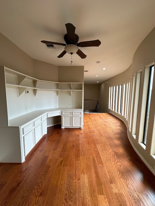 unfurnished office with ceiling fan, built in desk, and light wood-type flooring