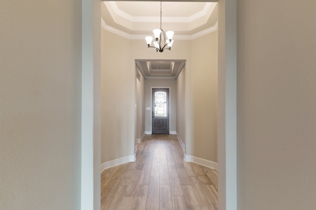 interior space with a tray ceiling, crown molding, an inviting chandelier, and light wood-type flooring