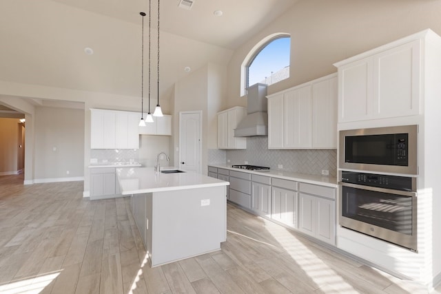 kitchen featuring appliances with stainless steel finishes, light wood-type flooring, a kitchen island with sink, high vaulted ceiling, and hanging light fixtures