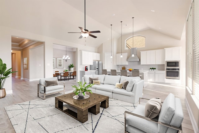 living room with ceiling fan with notable chandelier, light wood-type flooring, and high vaulted ceiling