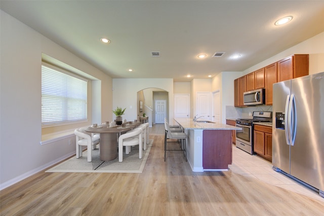 kitchen featuring appliances with stainless steel finishes, a kitchen breakfast bar, light stone counters, light hardwood / wood-style flooring, and an island with sink