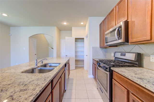 kitchen featuring decorative backsplash, light stone counters, sink, and appliances with stainless steel finishes