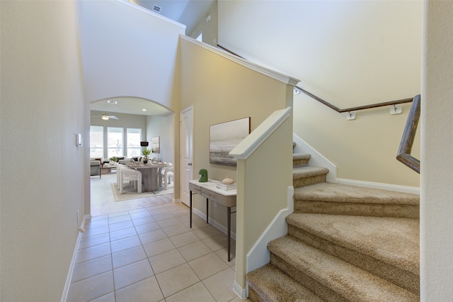 stairs with tile patterned floors, ceiling fan, and a towering ceiling