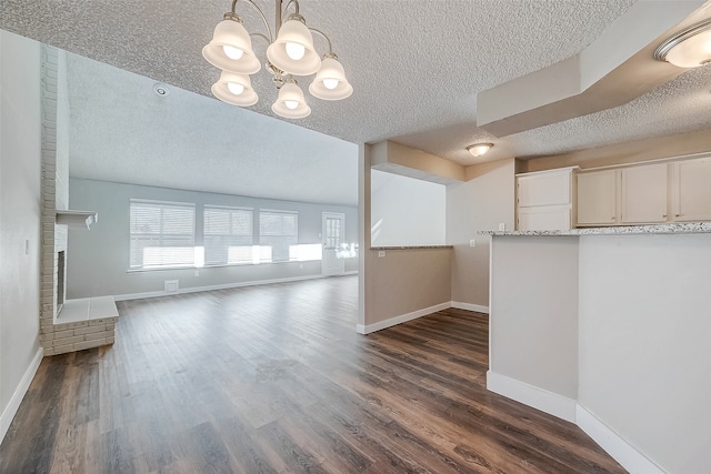 unfurnished living room with a textured ceiling, a notable chandelier, and dark wood-type flooring