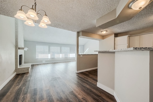 unfurnished living room featuring dark hardwood / wood-style floors, a chandelier, lofted ceiling, a textured ceiling, and a fireplace