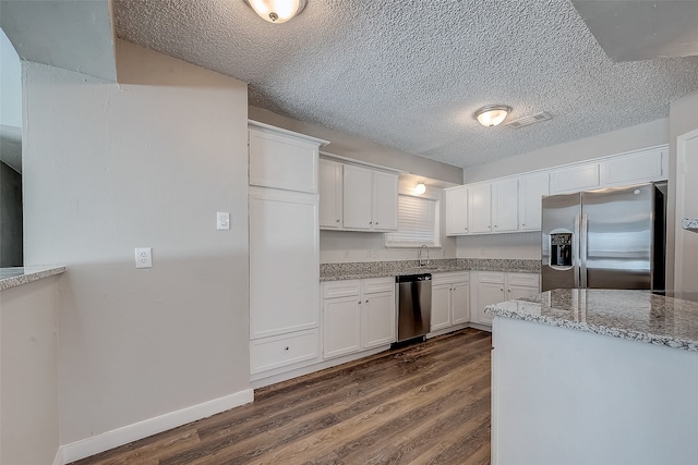 kitchen with light stone countertops, a textured ceiling, stainless steel appliances, dark wood-type flooring, and white cabinets