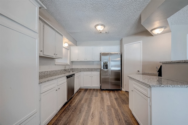 kitchen with white cabinetry, stainless steel appliances, light stone counters, and wood-type flooring