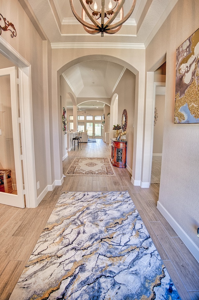 corridor featuring a raised ceiling, an inviting chandelier, light hardwood / wood-style flooring, and ornamental molding