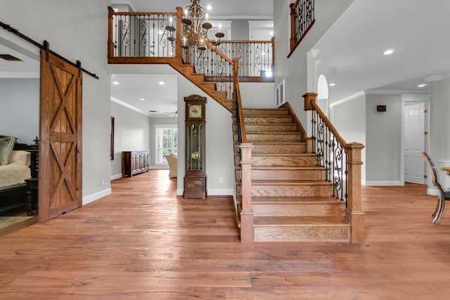 staircase featuring a barn door, hardwood / wood-style floors, a notable chandelier, and ornamental molding