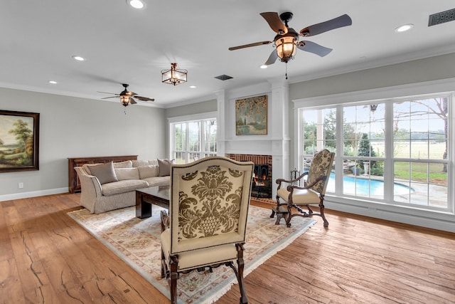 living room featuring light wood-type flooring, a brick fireplace, ceiling fan, and ornamental molding