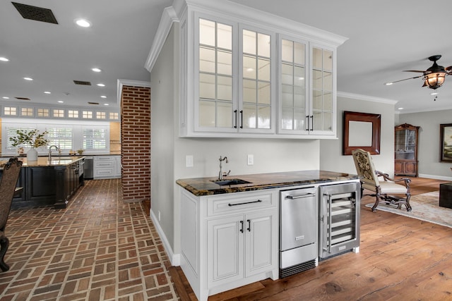 bar with dark hardwood / wood-style flooring, dark stone counters, beverage cooler, crown molding, and white cabinets