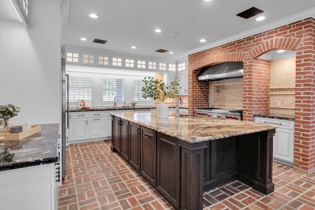 kitchen featuring exhaust hood, sink, ornamental molding, dark brown cabinets, and brick wall