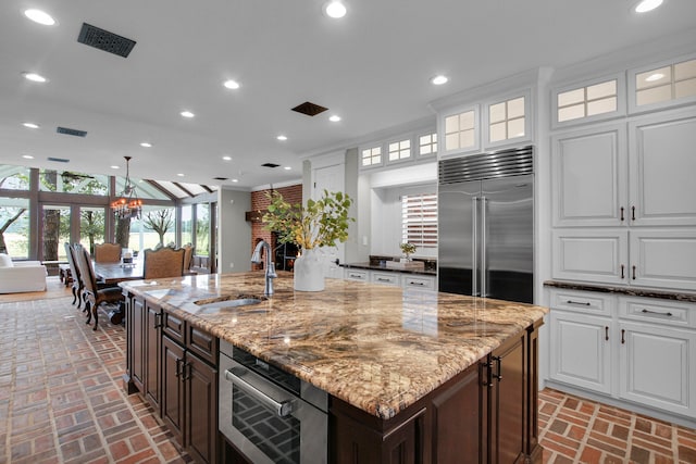 kitchen featuring white cabinets, built in refrigerator, a kitchen island with sink, and sink