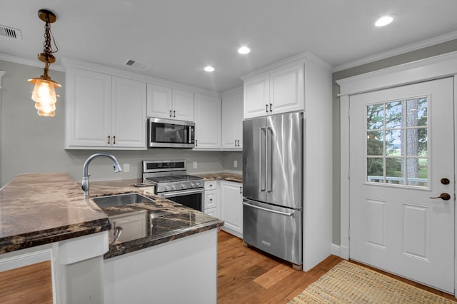 kitchen with kitchen peninsula, appliances with stainless steel finishes, light hardwood / wood-style floors, white cabinetry, and hanging light fixtures