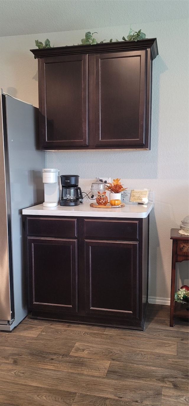 bar with dark hardwood / wood-style floors, stainless steel fridge, and dark brown cabinetry