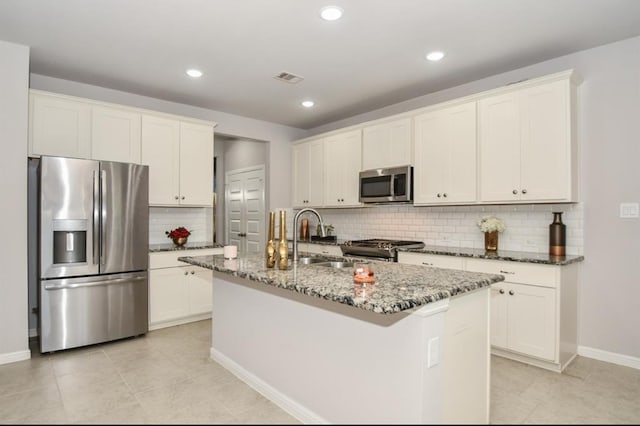 kitchen featuring sink, dark stone countertops, decorative backsplash, a center island with sink, and appliances with stainless steel finishes