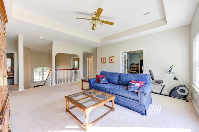 living room with a raised ceiling, light carpet, and ceiling fan