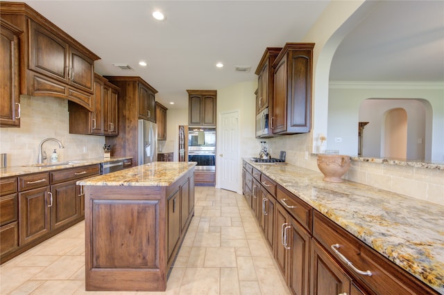 kitchen with a center island, crown molding, light stone countertops, appliances with stainless steel finishes, and tasteful backsplash