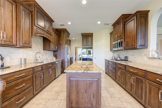 kitchen featuring backsplash, sink, light stone countertops, appliances with stainless steel finishes, and a kitchen island