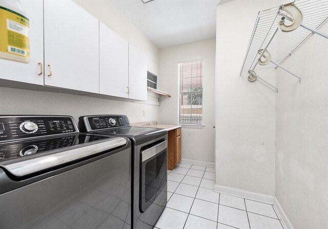 clothes washing area featuring washer and dryer, light tile patterned flooring, and cabinets