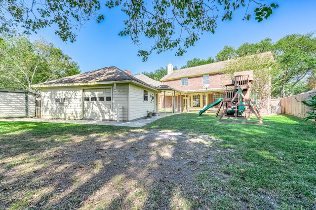 back of property featuring a playground, a lawn, an outdoor structure, and a garage