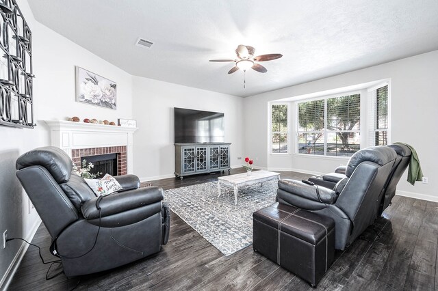 living room featuring a brick fireplace, ceiling fan, and dark wood-type flooring