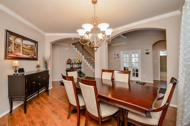 dining area featuring wood-type flooring, french doors, ornamental molding, and a notable chandelier