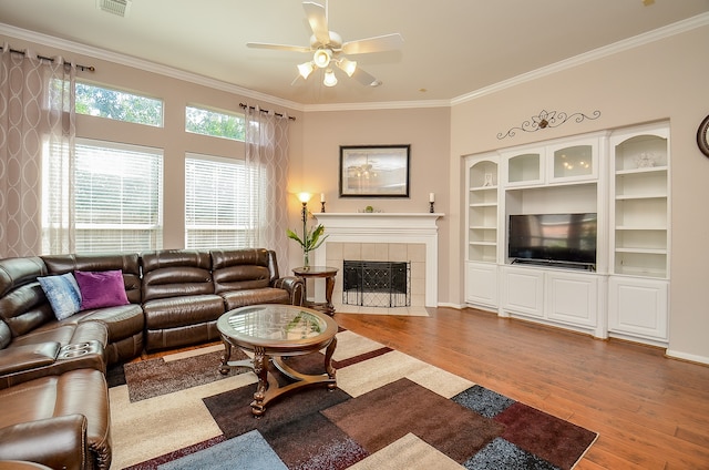 living room featuring a tiled fireplace, crown molding, hardwood / wood-style floors, and ceiling fan