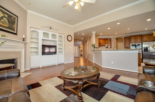 living room with ceiling fan, light hardwood / wood-style floors, ornamental molding, and a tiled fireplace