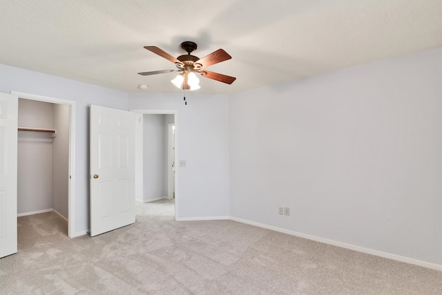 unfurnished bedroom with ceiling fan, a spacious closet, light carpet, and a closet