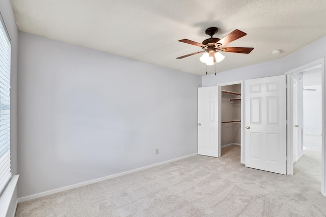 unfurnished bedroom featuring ceiling fan, a textured ceiling, a walk in closet, light carpet, and a closet