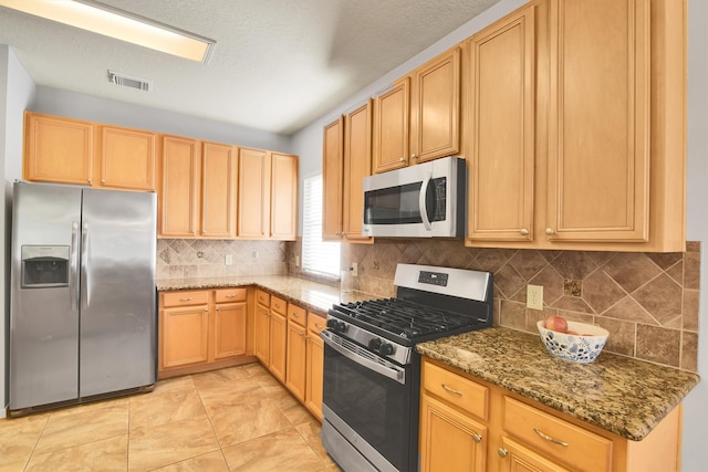 kitchen with tasteful backsplash, dark stone countertops, a textured ceiling, light tile patterned floors, and appliances with stainless steel finishes