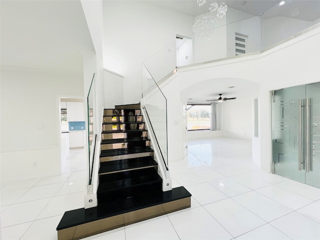 stairway featuring tile patterned flooring, ceiling fan with notable chandelier, and a towering ceiling