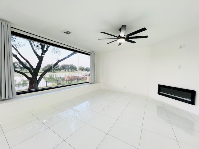 unfurnished room with light tile patterned floors, a water view, and ceiling fan