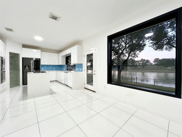 kitchen featuring decorative backsplash, stainless steel appliances, a water view, white cabinets, and a kitchen island