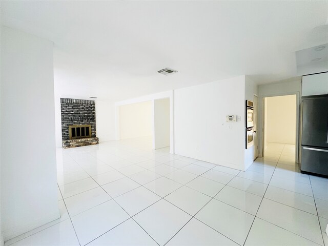 tiled spare room featuring a brick fireplace