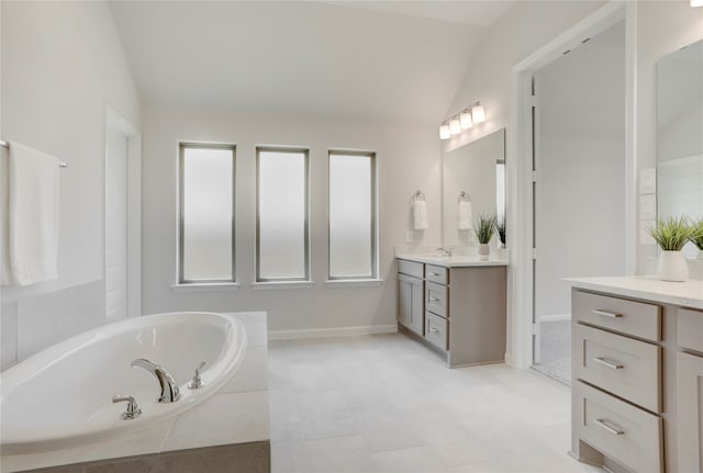 bathroom with vanity, a relaxing tiled tub, and vaulted ceiling