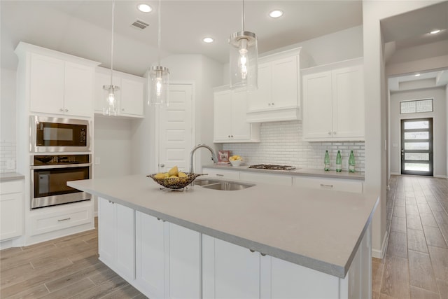 kitchen featuring a kitchen island with sink, white cabinets, hanging light fixtures, sink, and appliances with stainless steel finishes