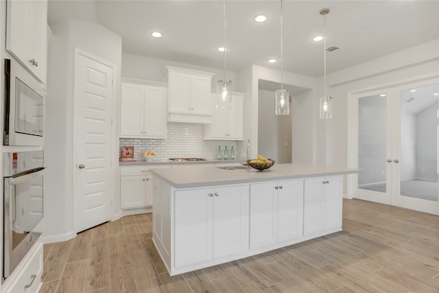 kitchen featuring white cabinets, oven, light hardwood / wood-style floors, and a center island with sink