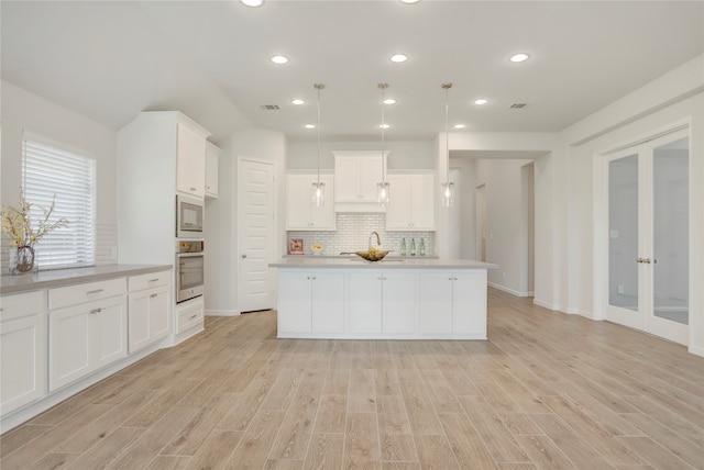 kitchen with stainless steel appliances, white cabinets, pendant lighting, and light wood-type flooring