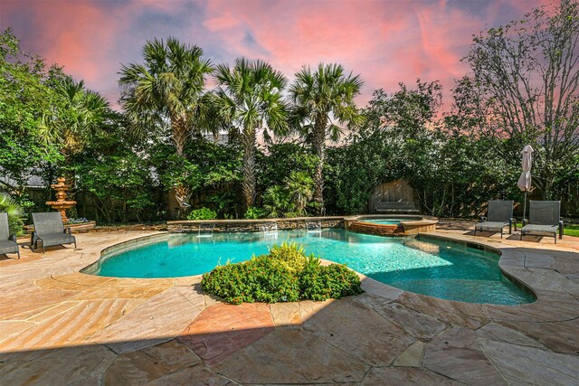 pool at dusk featuring an in ground hot tub and a patio area