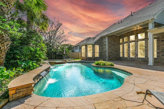 pool at dusk with an in ground hot tub, pool water feature, and a patio