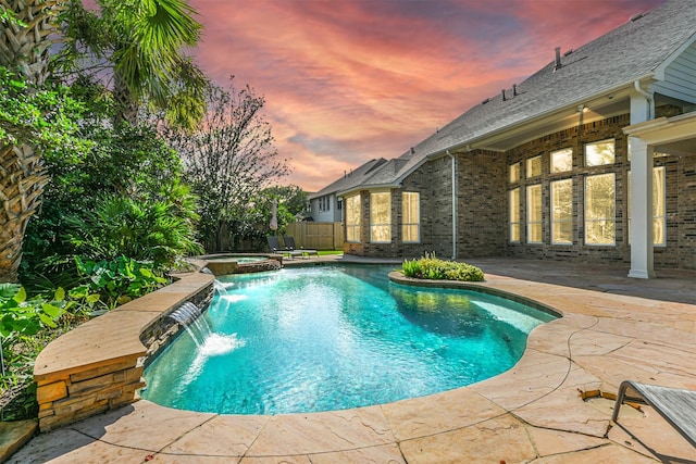 pool at dusk with an in ground hot tub, pool water feature, and a patio area