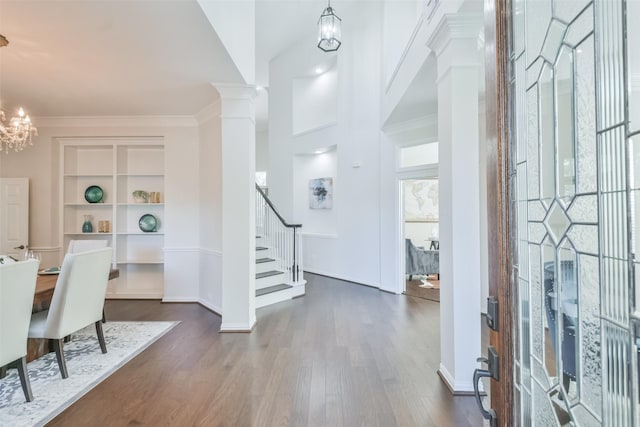 entryway featuring crown molding, a chandelier, dark wood-type flooring, and ornate columns