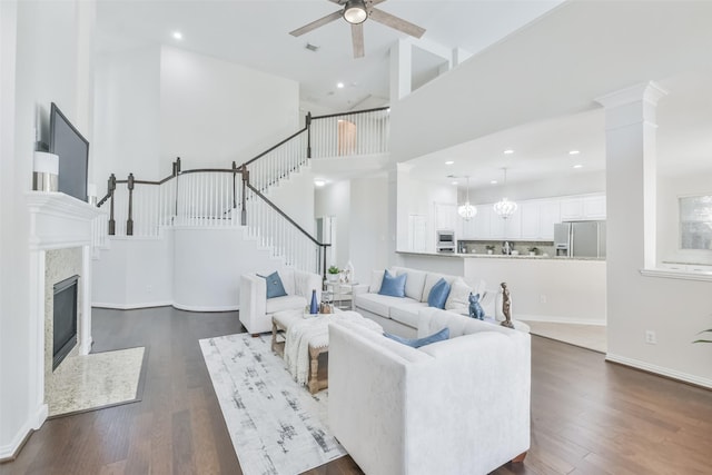 living room featuring a premium fireplace, dark hardwood / wood-style floors, ceiling fan with notable chandelier, and a towering ceiling