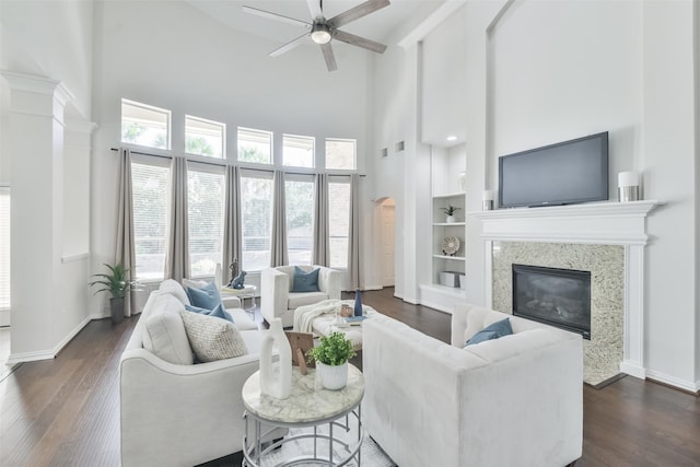 living room featuring built in features, dark hardwood / wood-style flooring, a high ceiling, ceiling fan, and a premium fireplace